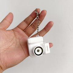 White compact digital camera on keychain with LCD screen and 32GB card.